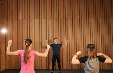 Instructor guiding two women in a gym workout session. Indoor fitness training.