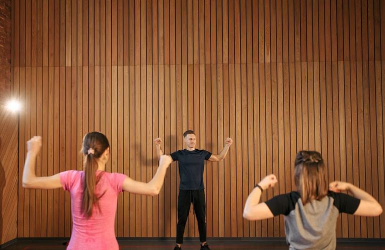 Instructor guiding two women in a gym workout session. Indoor fitness training.